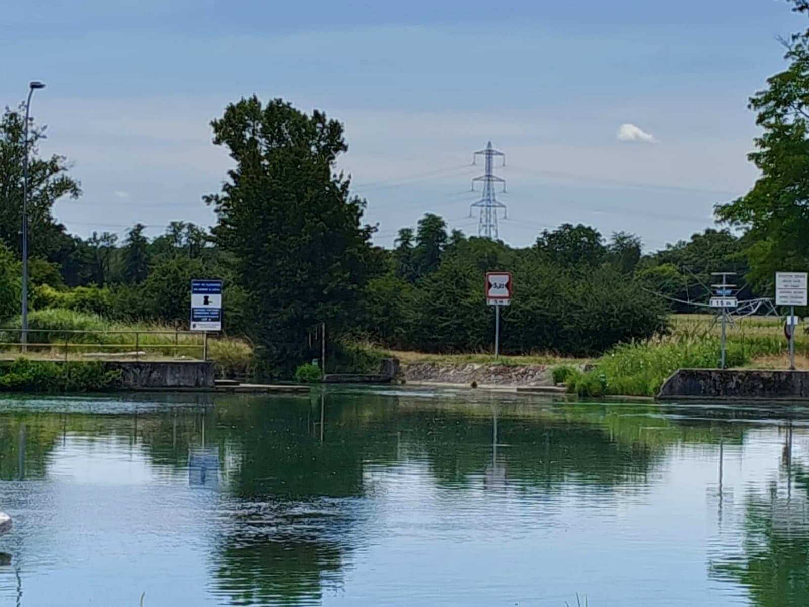 Le canal bordé d’arbres à hauteur du port de plaisance, panneaux de signalisation fluviale sur la berge