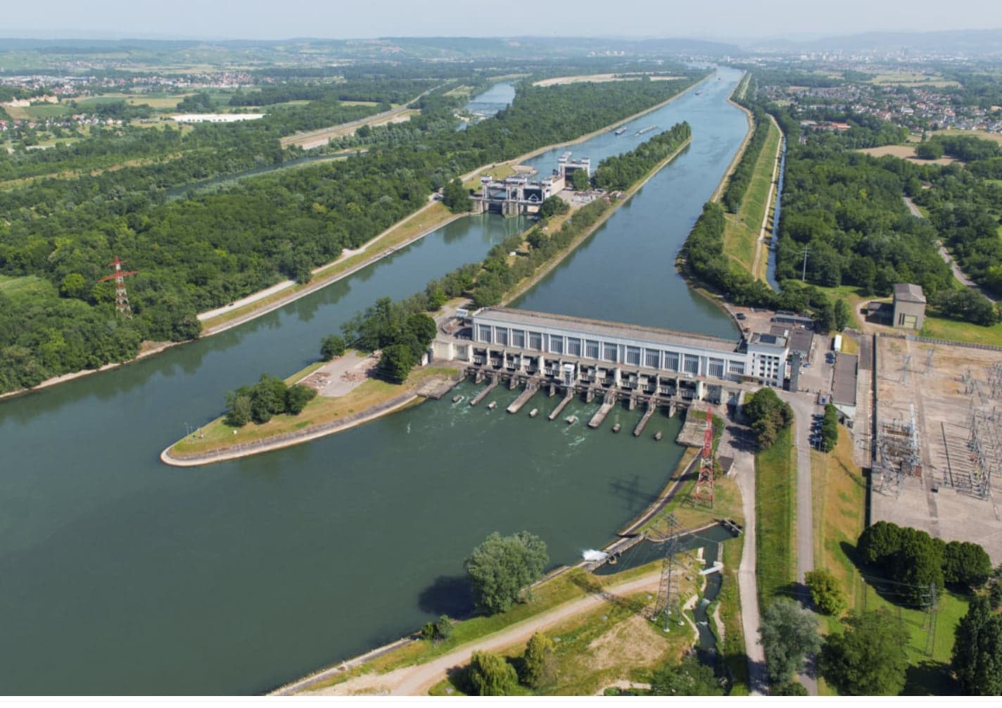 Vue aérienne de la centrale hydroélectrique de Kembs sur le Rhin, avec le long bâtiment des turbines, ses vannes ouvertes sur le fleuve, le Grand Canal d’Alsace et les écluses en amont