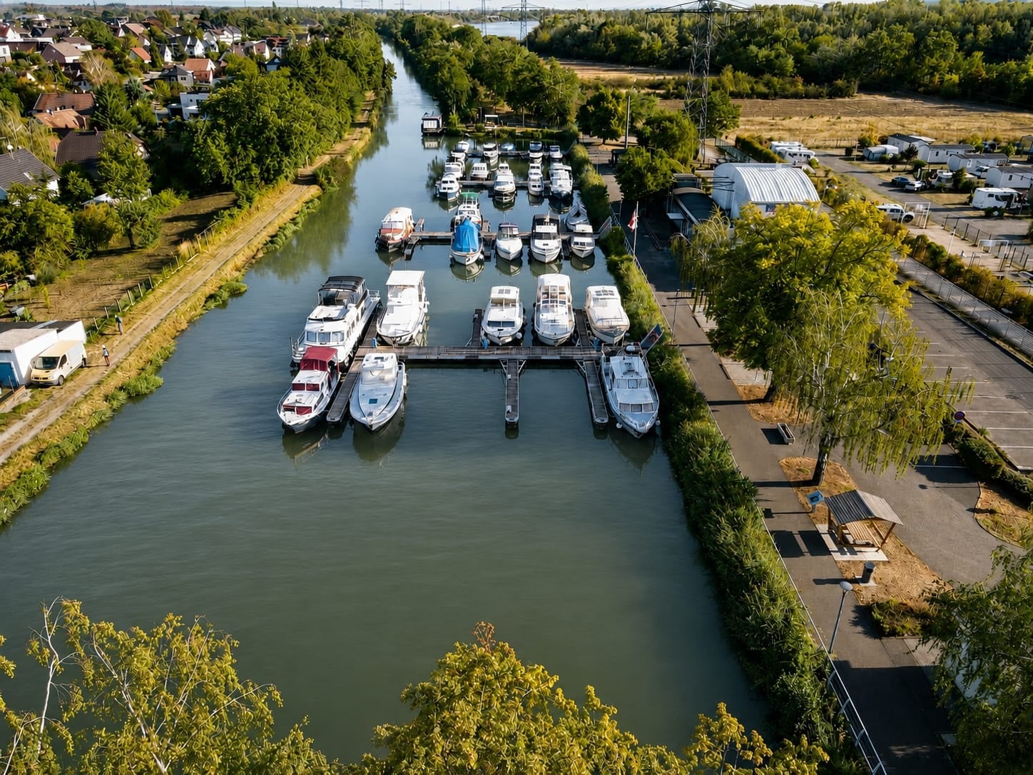 Vue aérienne du port de plaisance de Kembs : les bateaux amarrés le long des pontons, le canal bordé d’arbres et le village