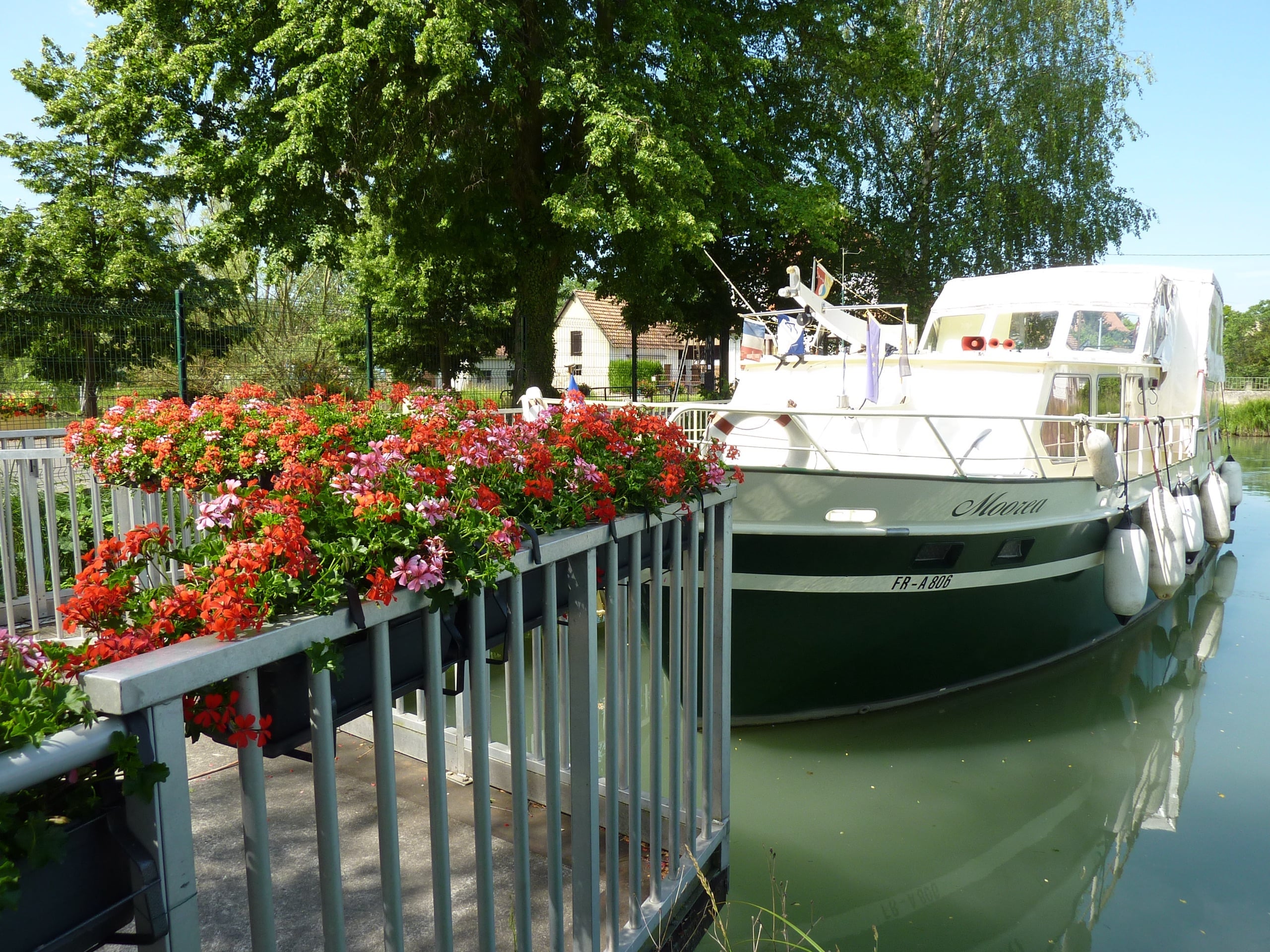 Pontons fleuris de géraniums rouges et bateau de plaisance amarré au port de Kembs